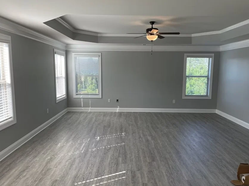A spacious, open living area in an Alpharetta, GA home featuring freshly painted gray walls, crisp white detailed crown molding, matching baseboards, and light gray wood-plank flooring.