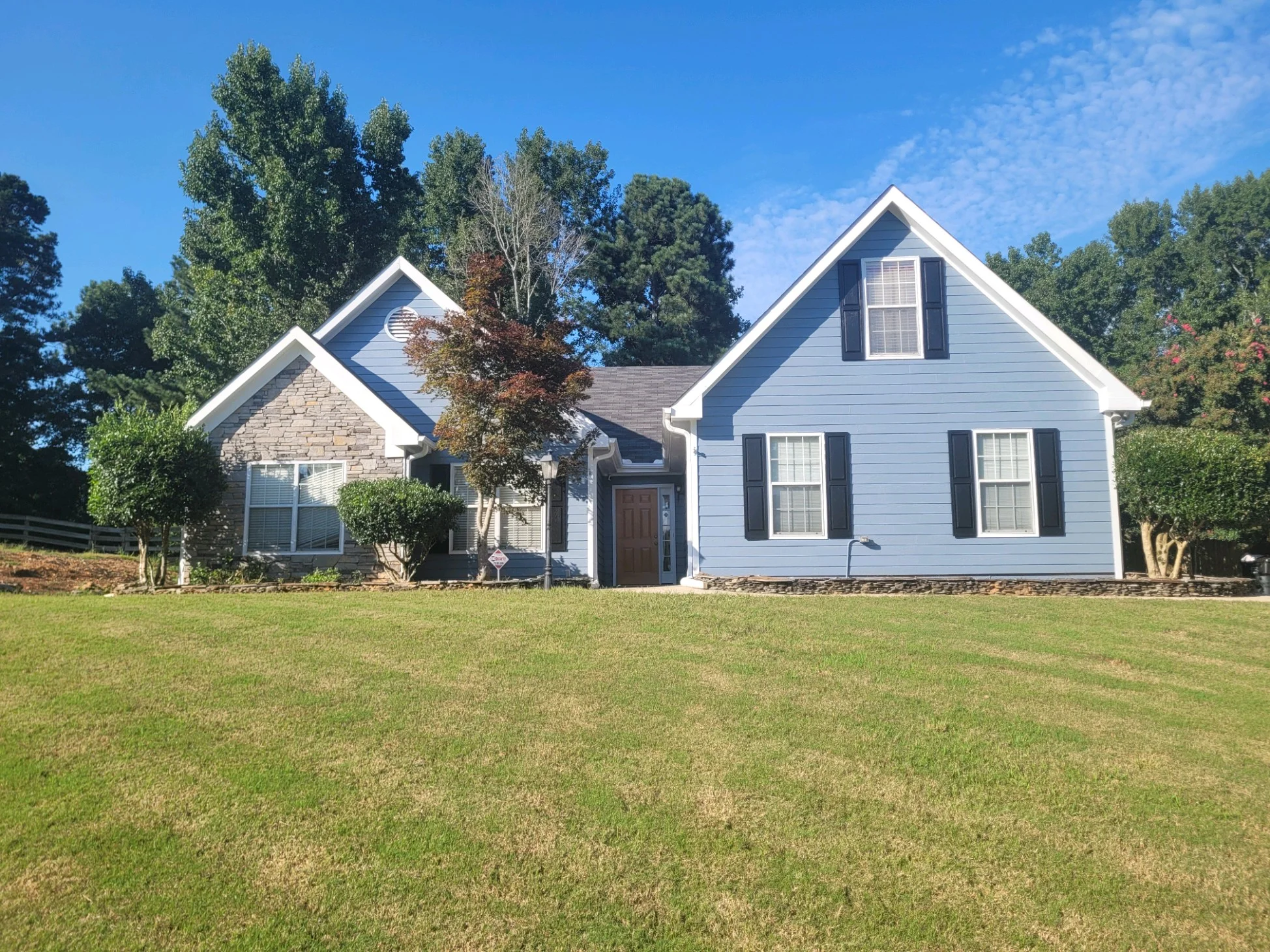 A multi-gabled Dacula, GA home showcasing common exterior surfaces including light blue fiber cement siding, a decorative stone facade, and dark black window shutters.