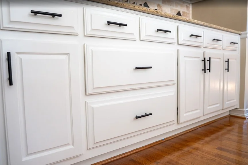 Cleanly coated white kitchen cabinets with modern black T-bar handles and hardware, showcasing the high-quality finish and surface protection provided by professional interior painting services in Alpharetta, GA.