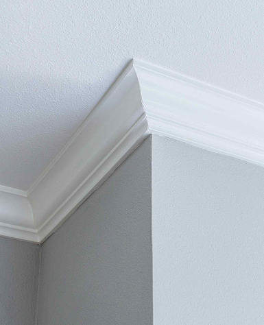 A clean corner of an interior room shows white crown molding and a smooth transition between gray walls and a white ceiling, conveying a modern look.