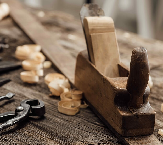 A vintage wooden hand plane on a rustic workbench with wood shavings, evoking a sense of craftsmanship and tradition in woodworking.