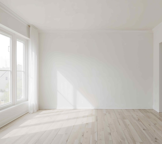 Bright, empty room with light wooden floors and large windows. Sunlight streams in, casting soft shadows. The atmosphere is serene and airy.