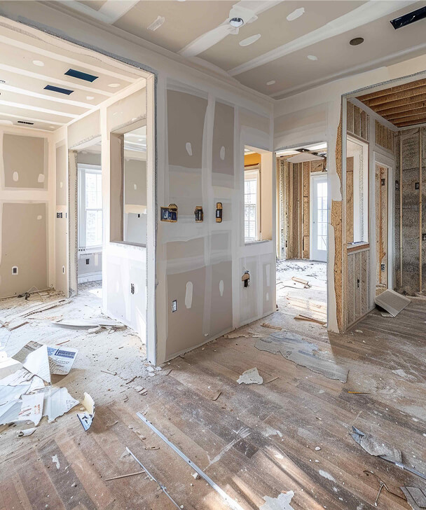 Partially constructed room with exposed drywall and electrical outlets. Sunlight streams in through windows, illuminating scattered debris on the floor.