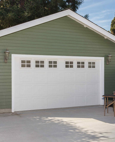 A quaint light gray garden shed with white trim, brown shingled roof, and double doors, surrounded by lush green grass and a gravel border.