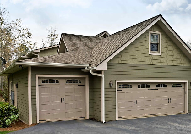 A suburban house with two taupe garage doors and olive siding. It's set against a cloudy sky.