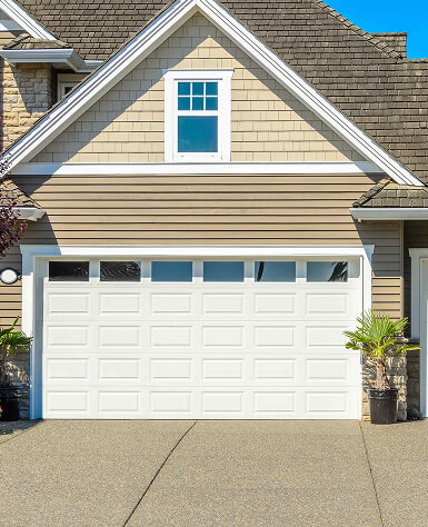 A modern house garage with a white door featuring small windows at the top. The siding is beige, and small potted plants flank the entrance. Bright and sunny.