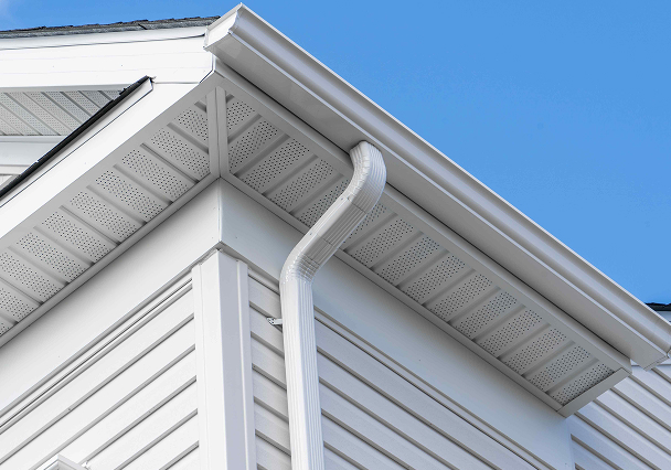 Rooftop corner of a white house with vinyl siding, showcasing a clean, white rain gutter system against a clear blue sky, conveying a crisp, neat appearance.