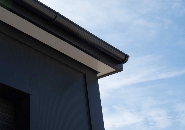Close-up of a modern building’s corner featuring a sleek black gutter against a clear blue sky, emphasizing contemporary architecture and clean lines.