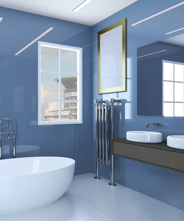 Modern bathroom with glossy blue walls, large window, white freestanding tub, dual sinks on a dark counter, and a gold-framed mirror. Bright and sleek.