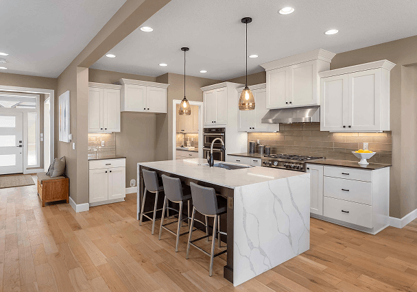 A modern kitchen with white cabinetry, a marble island, and gray countertops. Pendant lights hang above, and wooden floors add warmth to the decor.