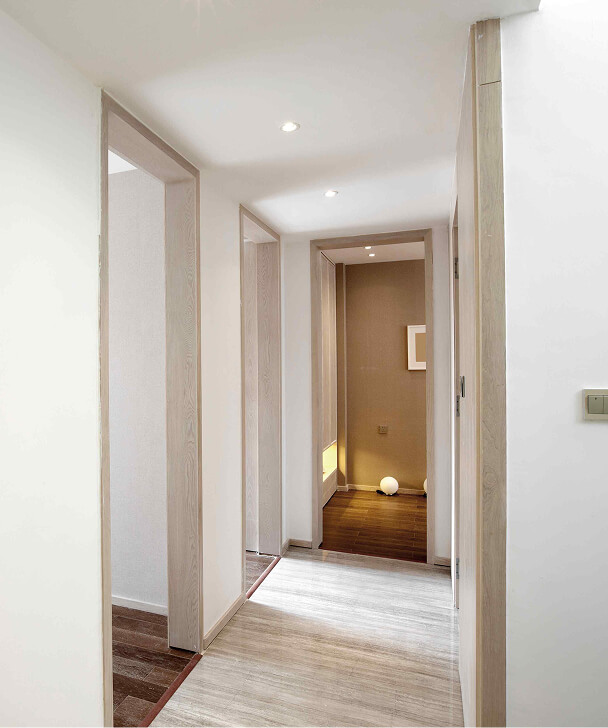 Minimalist hallway with light wood flooring and soft white walls. Warm, recessed lighting and a glowing orb create a calm, serene ambiance.