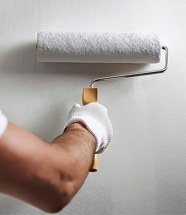 A gloved hand uses a paint roller to apply white paint on a textured wall, conveying a sense of freshness and renewal.
