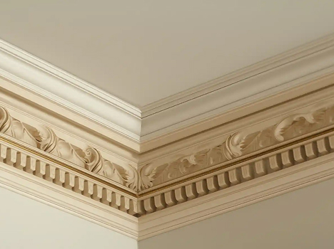Ornate beige crown molding decorates a room's corner, featuring intricate leaf designs and a ribbed pattern, evoking a classic, elegant feel.